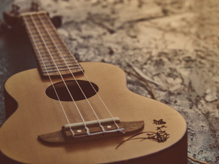 Ukulele positioned on left side of frame, soft warm matte tones, subtle travel mood, gentle light highlighting wood texture, open space on top right for text, artistic and cozy composition.の写真素材