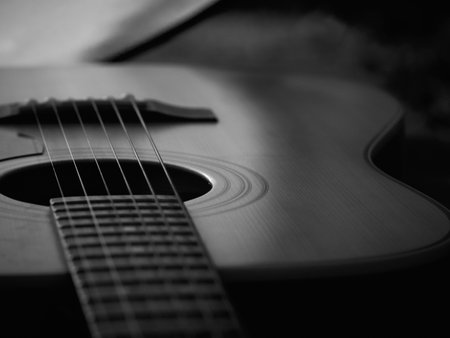 Monochrome photo of guitar with neck extending left, few frets in focus, rest of instrument softly blurred, light highlighting center and upper body, right side out of focus, moody and slightly melancholic atmosphere.の写真素材