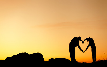 Conceptual heart shape, symbol of human. Woman and man hand silhouette over sky at sunset background, metaphor to love, valentine day, romantic, couple, wedding, romance, summer or sunriseの写真素材