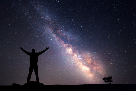 Milky Way. Night sky with stars and silhouette of a man with raised-up arms.の写真素材