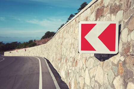 Asphalt road in autumn forest at sunrise and road sign. Crimean mountains.