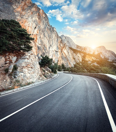 Beautiful winding mountain road with a perfect asphalt with high rocks and colorful sunset in summer.の写真素材