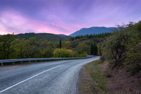 Mountain winding road passing through the forest with colorful sky at sunset in summerの写真素材