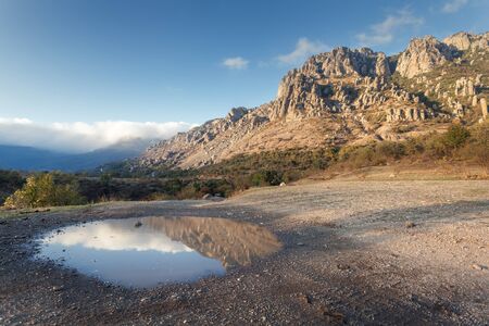 Mountain landscape with blue sky reflection in puddle at sunset.