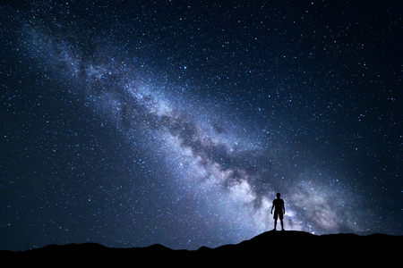 Landscape with Milky Way. Night sky with stars and silhouette of a standing happy man on the hill.の写真素材