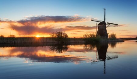 Landscape with beautiful traditional dutch windmills near the water canals with blue sky and clouds reflection in water. Colorful yellow sunrise in famous Kinderdijk, Netherlands in springの写真素材