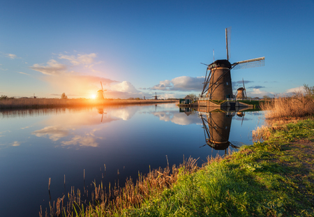 Beautiful traditional dutch windmills near the water channels with reflection in water at colorful sunrise in famous Kinderdijk, Netherlandsの写真素材