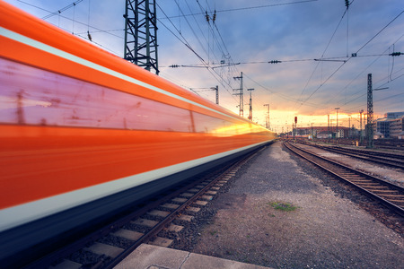 High speed red passenger train on railroad track in motion at sunset. Blurred commuter train. Railway station with cloudy sky. Railroad travel, railway tourism. Industrial landscape. Vintage toningのeditorial素材