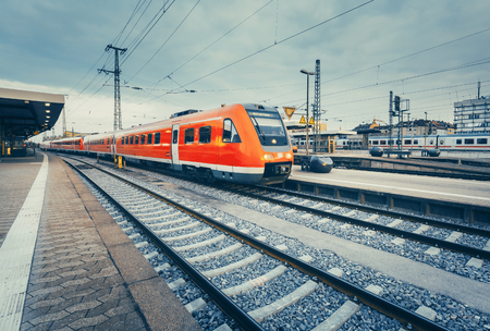 Beautiful railway station with modern high speed red commuter train at colorful sunset. Railroad with vintage toning. Train at railway platform. Industrial concept.のeditorial素材