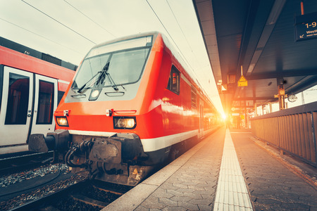 Modern high speed red commuter train at colorful sunset. Beautiful railway station. Railroad with vintage toning. Train at railway platform. Industrial concept. Railway tourismのeditorial素材