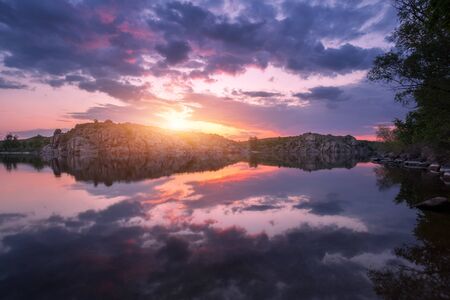River against colorful sky with clouds and rocks at sunset in summer. Beautiful landscape with lake,...