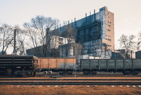 Railway station with freight wagons and train against metallurgical plant at sunset. Colorful industrial landscape. Railroad with vintage toning. Railway platform. Heavy industry. Cargo shippingの写真素材