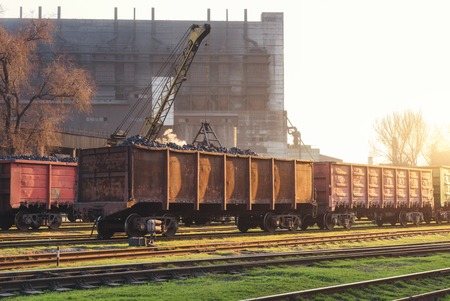 Railway station with freight wagons and train against metallurgical plant at sunset. Colorful...
