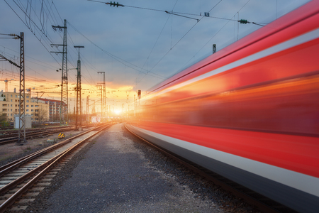 High speed red passenger train on railroad track in motion at sunset. Blurred commuter train on the railway station and sunlight. Railroad travel, railway tourism. Industrial landscape in Germanyの写真素材