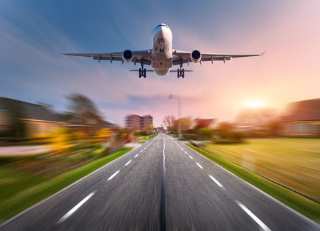 Passenger airplane with motion blur effect. Airplane is flying in the sunset sky over the rural asphalt road at sunset in Netherlands. Landing airplane with blurred background. Aircraft. Business tripの写真素材