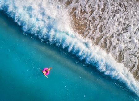 Aerial view of young woman swimming on the pink swim ring in the transparent turquoise sea in Oludeniz,Turkey. Summer seascape with girl, beautiful waves, azure water in sunny day. Top view from droneの写真素材