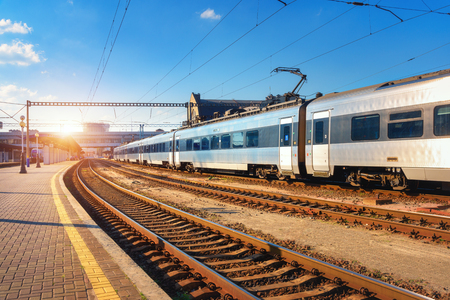 Beautiful passenger train at the railway station at sunset. Industrial view with modern intercity train, railroad, railway platform and blue sky in the evening. Railway tourism and transportationのeditorial素材
