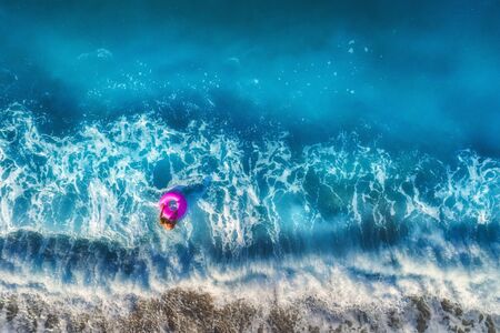 Aerial view of young woman with pink swim ring in the transparent turquoise sea in Oludeniz,Turkey. Summer seascape with girl, beautiful waves, blue water in sunny morning. Top view from drone. Travelの写真素材