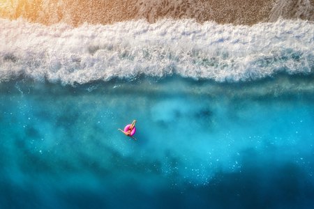 Aerial view of slim woman swimming on the pink swim ring in the transparent turquoise sea in Oludeniz,Turkey. Summer seascape with girl, beautiful waves, blue water in sunny day. Top view from droneの写真素材