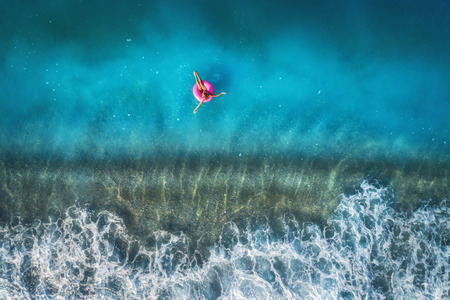 Aerial view of young woman swimming on the pink swim ring in the transparent turquoise sea in Oludeniz,Turkey. Summer seascape with girl, beautiful waves, blue water in sunny day. Top view from droneの写真素材