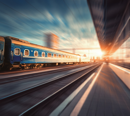 Beautiful train with blue wagons in motion at the railway station at sunset. Industrial view with...
