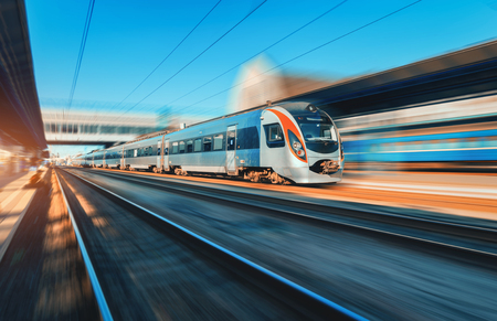 High speed train in motion at the railway station at sunset in Europe. Modern intercity train on the railway platform with motion blur effect. Industrial scene with moving passenger train on railroadのeditorial素材