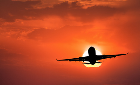 Silhouette of aircraft and orange sky with sun. Landscape with passenger airplane is flying in the sky with clouds at sunset. Travel background. Passenger airliner. Commercial airplane. Businessの写真素材