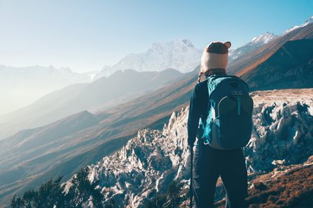 Standing young woman with backpack on the mountain peak and looking on beautiful mountain valley at sunset. Landscape with girl, rocks with snowy peaks, hills, blue sky in Nepal.Hiking, travel.Vintageの写真素材