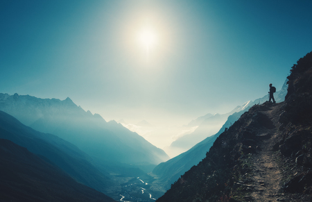 Standing woman on the hill against mountain valley at bright sunny day. Landscape with girl, trail, mountain, blue sky with sun and low clouds at sunset in Nepal.  Lifestyle, travel. Trekkingの写真素材