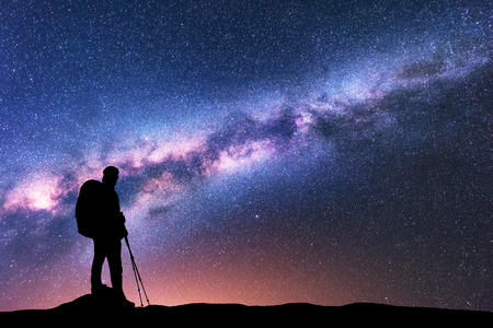 Silhouette of man with backpack and trekking poles against amazing purple Milky Way at night. Space. Landscape with man, bright milky way, sky with stars. Beautiful galaxy. Travel. Starry sky. Natureの写真素材