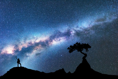 Milky Way, silhouette of woman and tree growing from the rock on the mountain at night. Space background with starry sky, beautiful galaxy and girl. Blue Milky Way, tree and woman. Universe. Adventureの写真素材