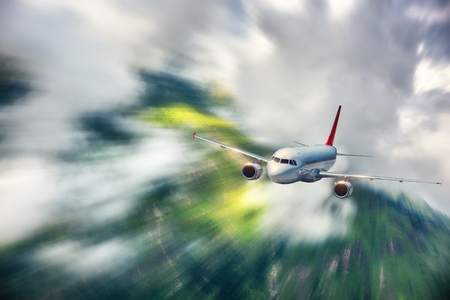 Modern airplane with motion blur effect is flying in clouds at sunset. Passenger airplane, blurred clouds, green forest. Passenger aircraft in motion. Business travel. Commercial plane.Conceptの写真素材