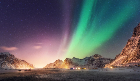 Green and purple aurora borealis over snowy mountains. Northern lights in Lofoten islands, Norway. Starry sky with polar lights. Night winter landscape with aurora, high rocks, beach. Travel. Natureの写真素材