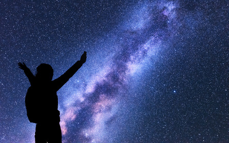 Milky Way with silhouette of a happy woman with backpack and raised up arms at night. Space background with sky with stars, bright colorful milky way, girl. Success. starry sky and woman. Night sceneの写真素材