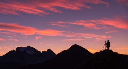 Silhouette of a photographer on the mountain peak against rocks and purple sky with pink clouds at sunset. Landscape with man, mountain ridge and colorful sky at dusk in Dolomites, Italy. Travelの写真素材