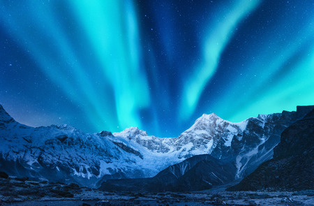 Aurora borealis above the snow covered mountain range in europe. Northern lights in winter. Night landscape with green polar lights and snowy mountains. Starry sky with aurora over the rocks. Spaceの写真素材