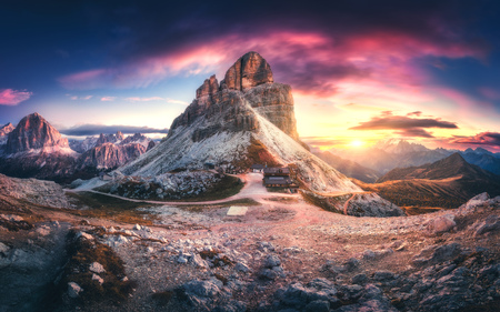 Mountain pass and beautiful sky with colorful clouds at sunset. Dramatic panoramic landscape with rocks, mountain peaks, stones, trails, buildings, trees on hills at dusk. Autumn in Dolomites, Italyの写真素材