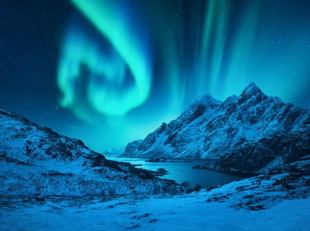 Aurora borealis above the snow covered mountains in Lofoten islands, Norway. Northern lights in winter. Night landscape with polar lights, snowy rocks, reflection in the sea. Starry sky with auroraの写真素材