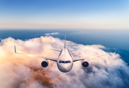 Airplane is flying over clouds at sunset in summer. Landscape with passenger  airplane, low clouds, sea, purple sky at dusk. Front view of the aircraft. Business travel. Commercial plane. Aerial viewの写真素材
