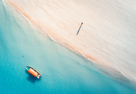 Aerial view of the fishing boat in clear blue water and man on the sandy beach at sunset in summer. Top view of boat. Indian ocean. Travel in Zanzibar, Africa. Landscape with motorboat, sea. Seascapeの写真素材