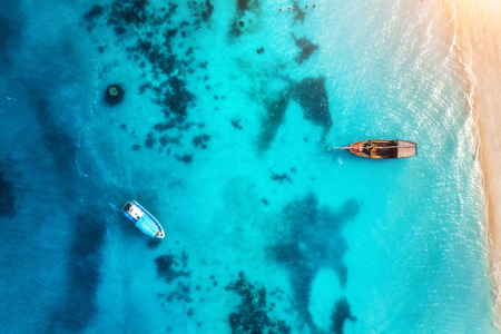 Aerial view of the fishing boats in transparent blue water at sunset in summer. Top view from of boat and sandy beach. Indian ocean in Zanzibar, Africa. Landscape with yachts and clear sea. Travelの写真素材