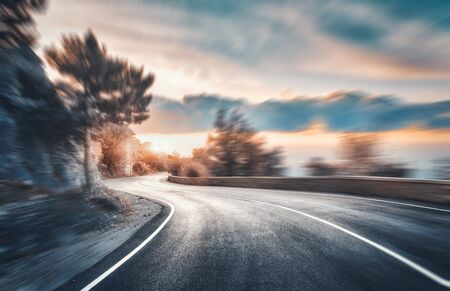 Mountain road at sunset with motion blur effect. Asphalt road and blurred background with rocks,...
