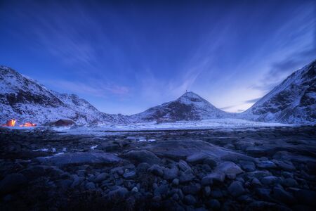 Blue sky with stars and clouds over rocky beach and snow covered mountains at night Lofoten islands,...