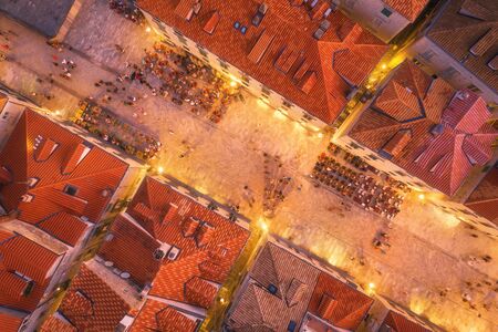 Aerial view of houses with red roofs at night in Dubrovnik, Croatia. Top view of beautiful architecture in old city. City lights, historical centre, buildings, walking people in illuminated streetsの写真素材