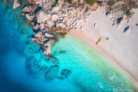 Aerial view of sandy beach with couple and canoe, sea with transparent blue water and rocks in sunny...