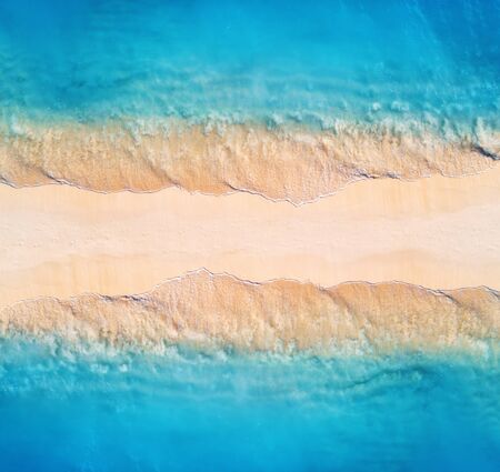 Aerial view of transparent blue sea with waves on the both sides and empty sandy beach at sunset....