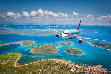 Airplane is flying over small islands and sea at sunny day in summer. Aerial view of passenger airplane, tropical seashore, mountains with green trees, sky and blue water. Top view of aircraft. Travelの写真素材