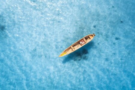 Aerial view of the fishing boat in transparent blue water at sunny day in summer. Top view from above of boat, sandy beach. Indian ocean in Zanzibar, Africa. Landscape with canoe and clear sea. Travelの写真素材