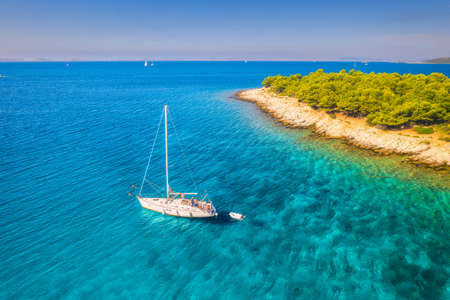 Aerial view of beautiful sailboat and small island in the sea at sunny day in summer in Croatia. Top view of transparent blue water, green trees, sandy beach, yachts. Tropical landscape with boatの写真素材