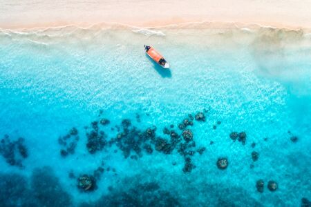Aerial view of alone fishing boat in transparent blue water at sunset in summer. Top view of boat from drone , sandy beach in Zanzibar. Travel. Tropical seascape with motorboat, sea. View from aboveの写真素材